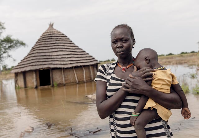 Abuk holds her child outside their flooded home in South Sudan.
